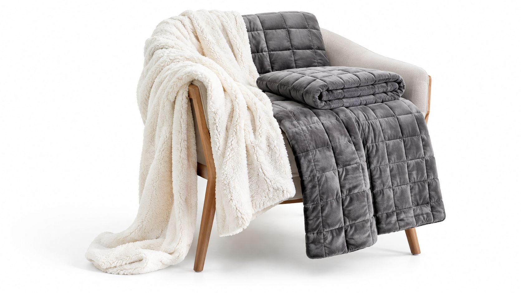 A light beige armchair draped with a soft cream-colored sherpa blanket and a grey weighted blanket.